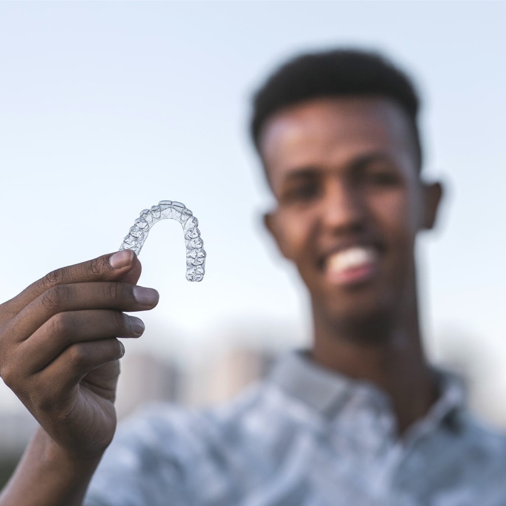 A man is holding up an Invisalign tray.