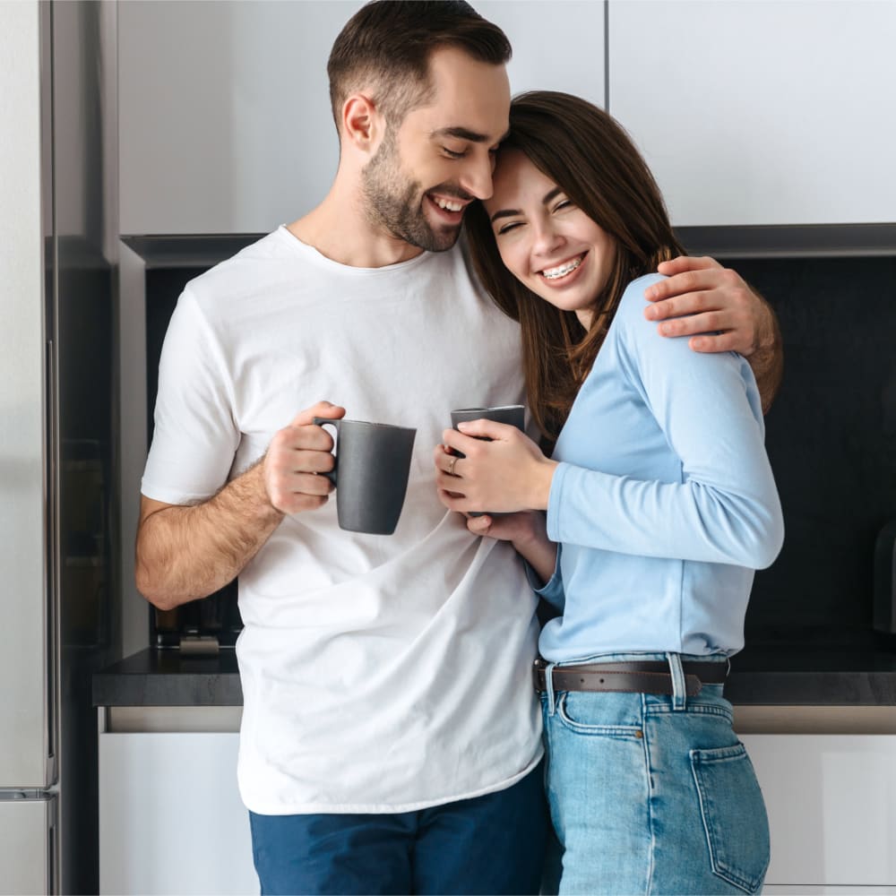 A man and a woman are embracing in a kitchen. She is smiling, showing off braces. Vancouver