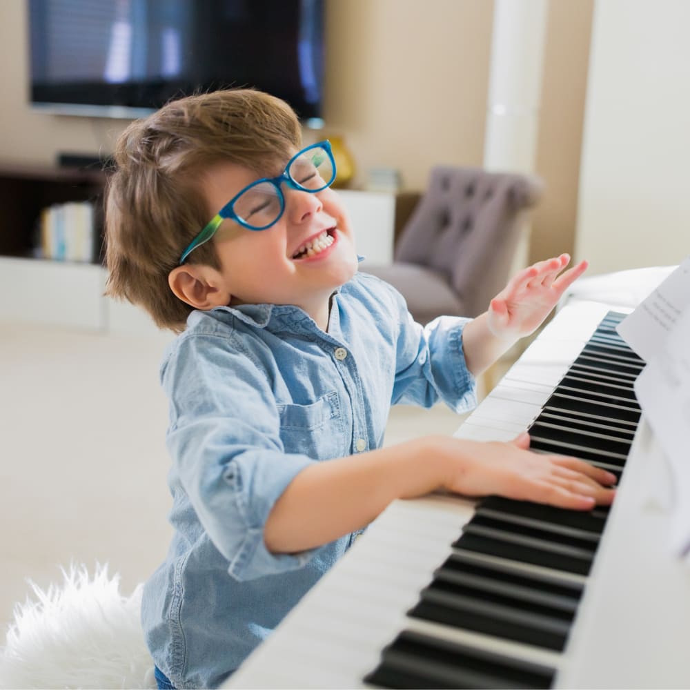 A young boy with blue glasses is playing on a piano.