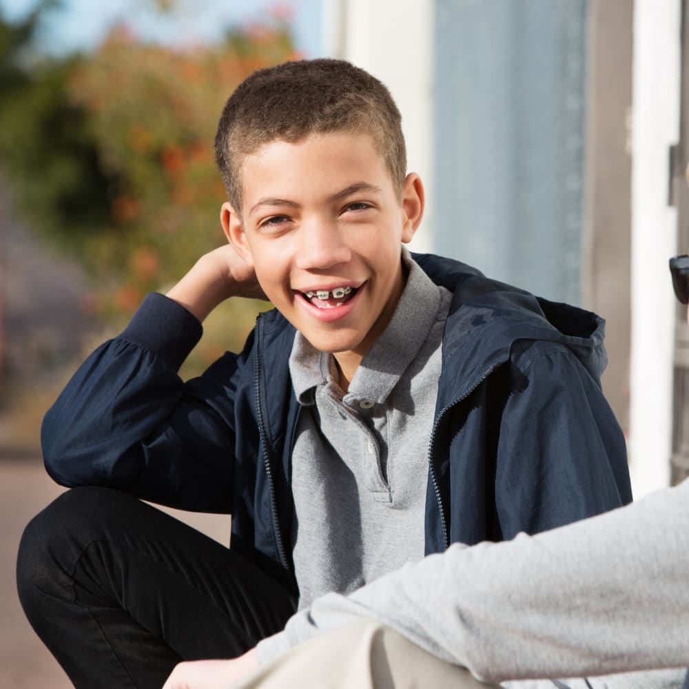 A young boy is sitting with his elbow on his knee, smiling.