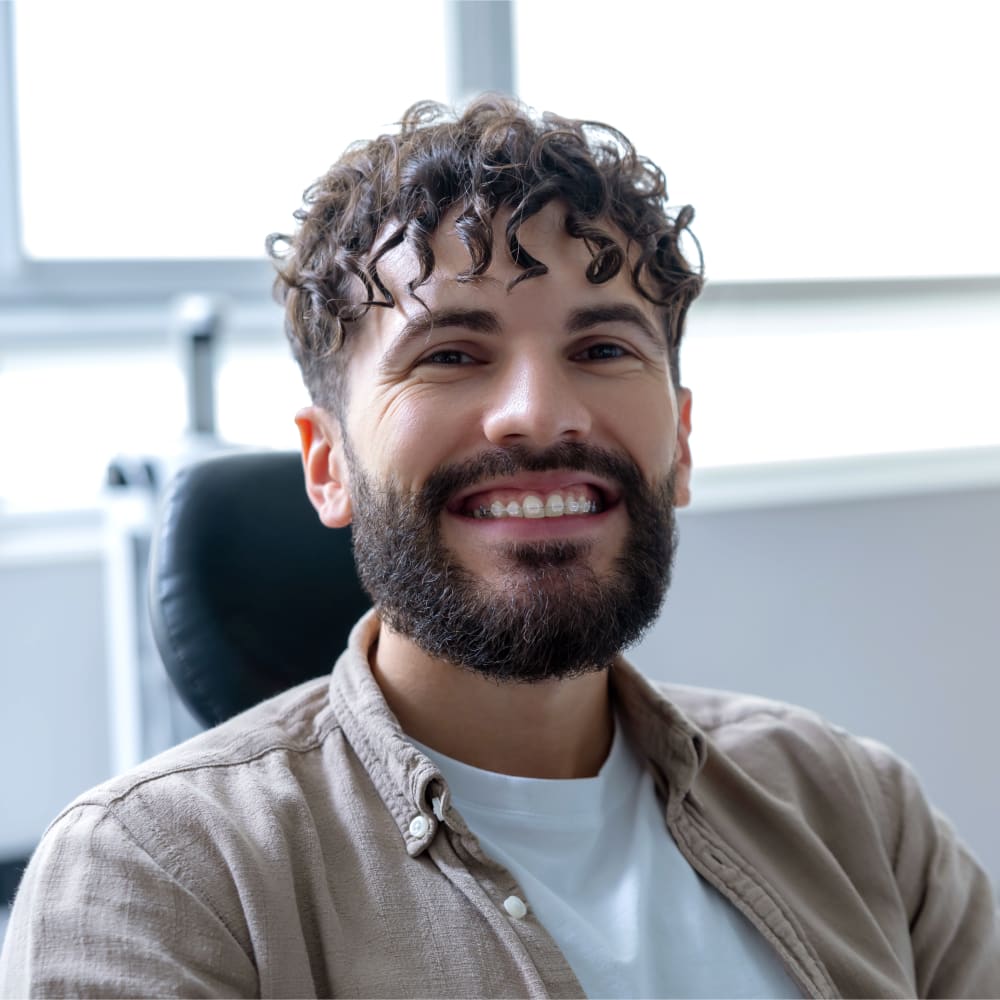 A man with curly hair is smiling. He has ceramic braces on.