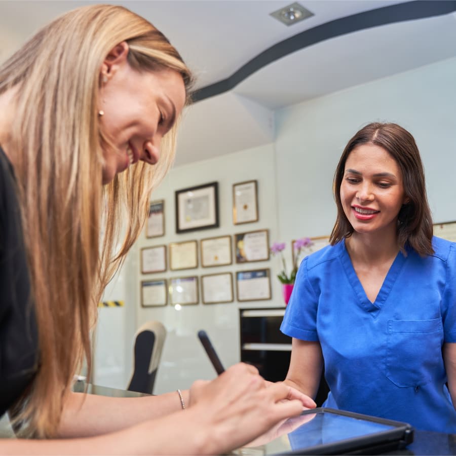 A dental assistant is smiling brightly as the patient fills out forms.
