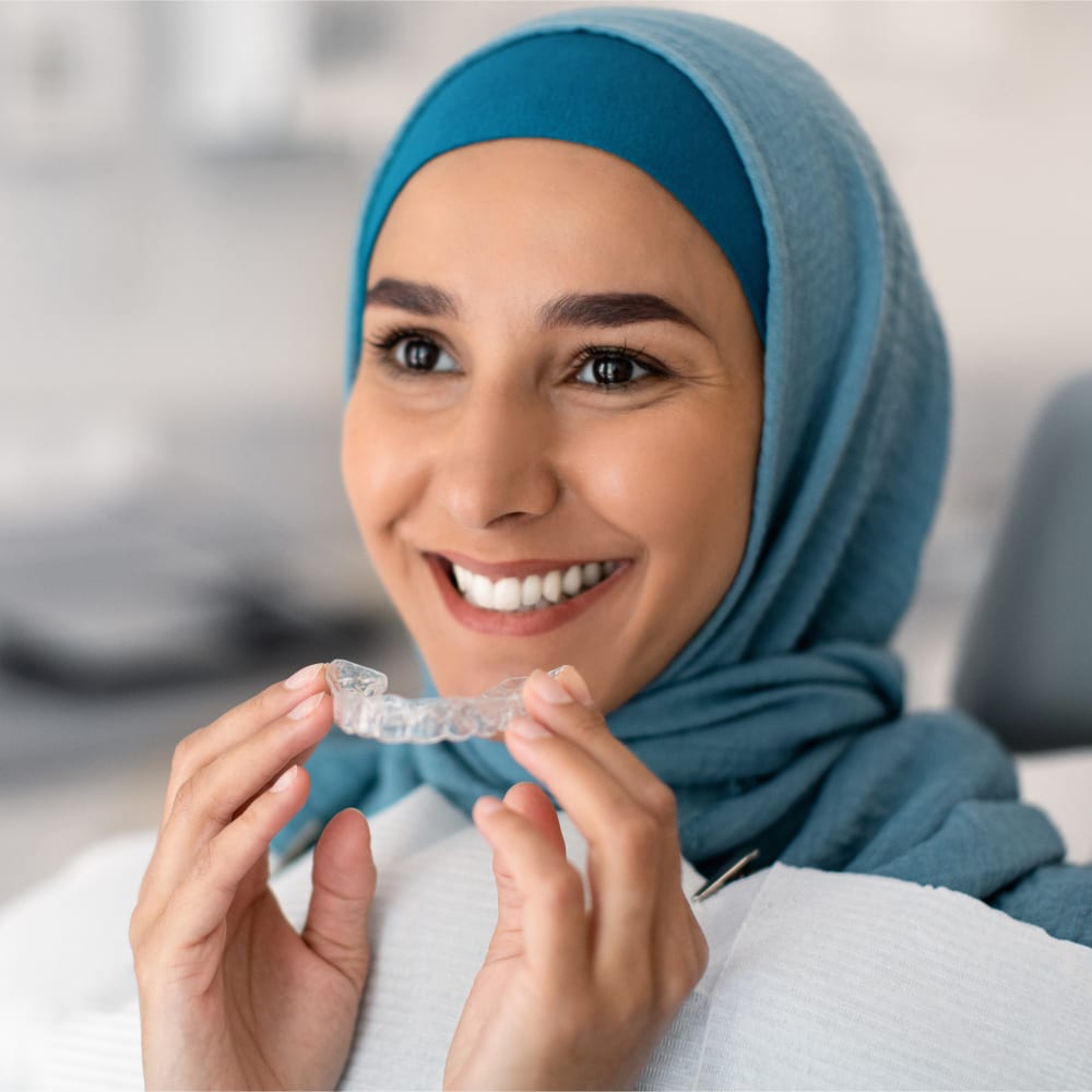 A woman in a blue scarf is holding Invisalign up to her mouth.