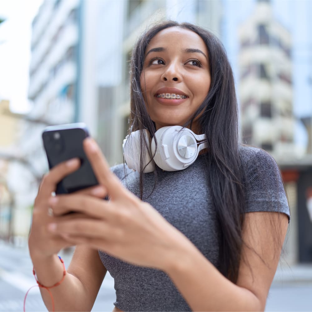 A teenage girl is using her smartphone and smiling, showing off her braces.