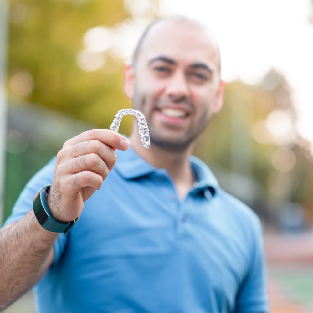 A man holds up an Invisalign tray.
