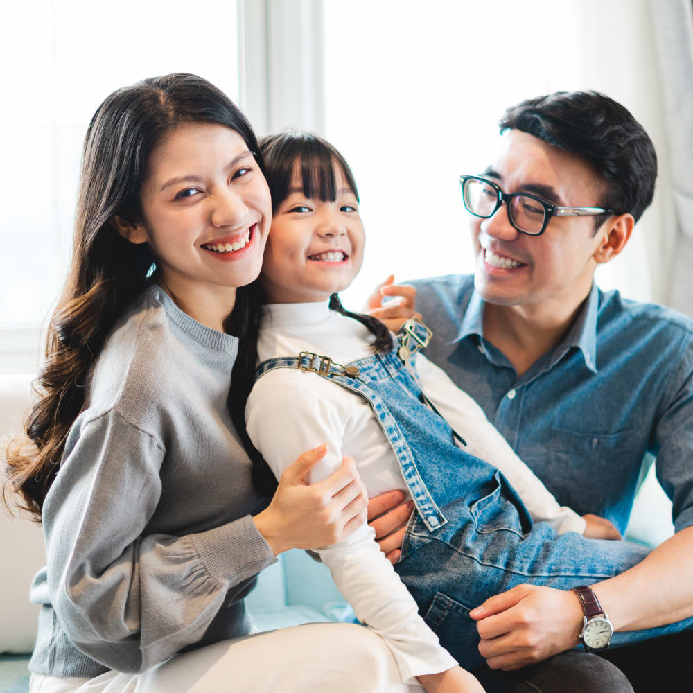 A young girl is sitting on her parent's laps smiling.