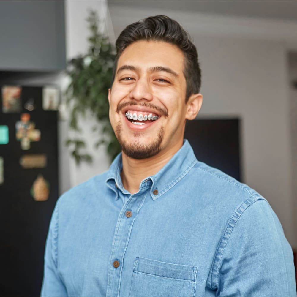 A man in a denim shirt is wearing braces and smiling.
