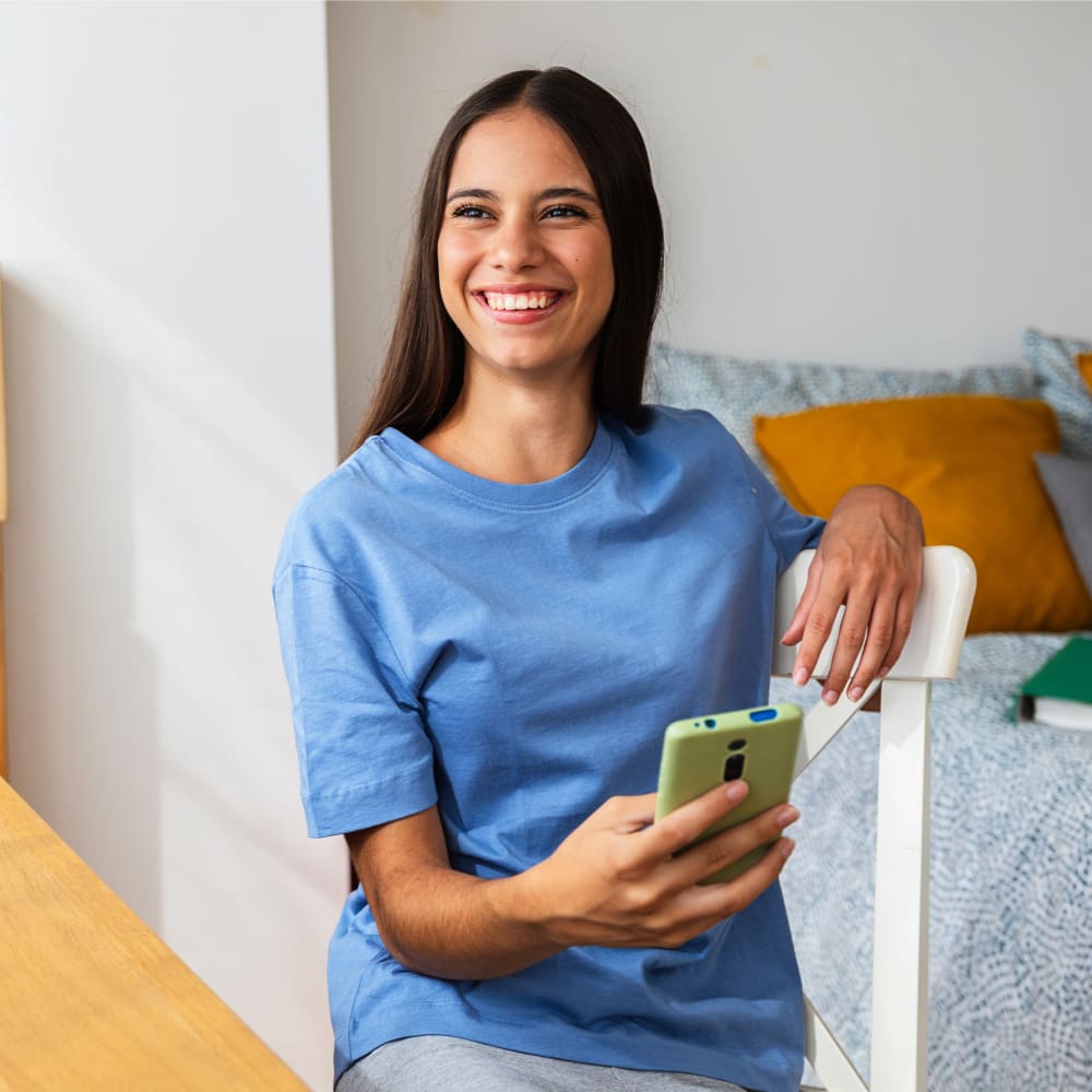 A girl with straight teeth is smiling and holding her phone.